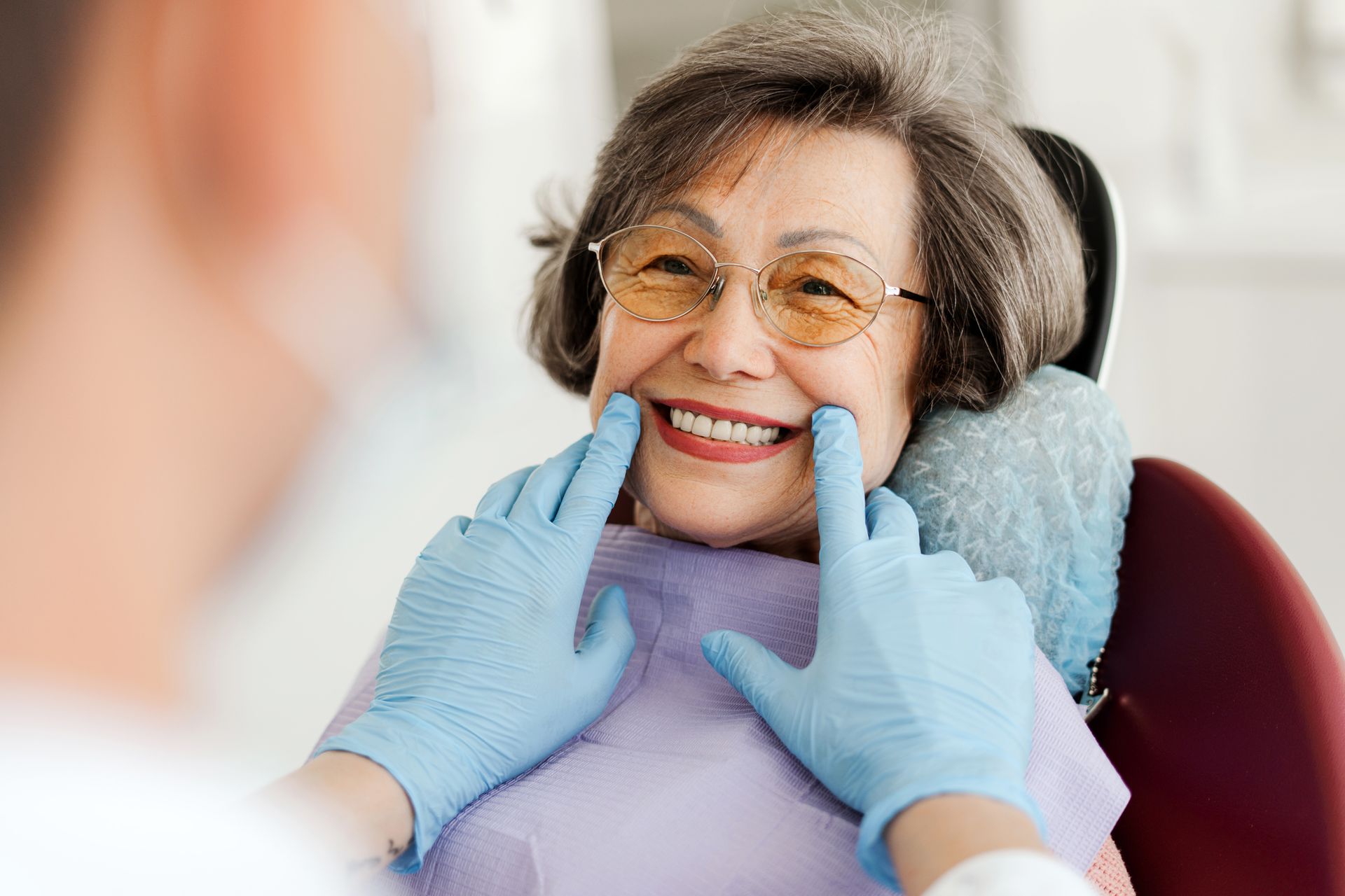 An elderly woman is smiling while sitting in a dental chair.
