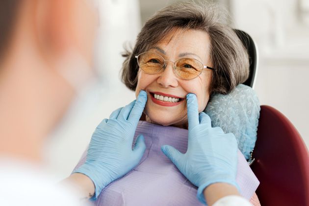 An elderly woman is smiling while sitting in a dental chair.