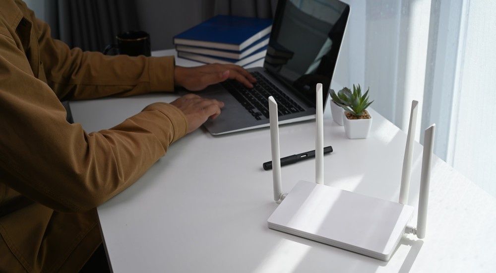 Person Working on A Laptop at A White Desk Next to A Wireless Router — Oz Data Tech in Taree, NSW