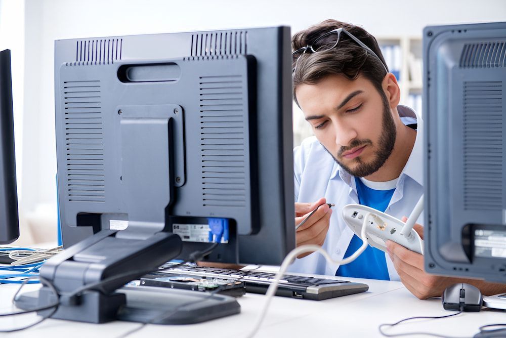 A Man Is Working On A Computer In Front Of Two Monitors — Oz Data Tech in Forster, NSW