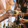 People pouring white wine into glasses at a lively indoor gathering