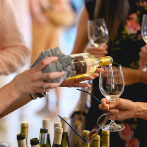 People pouring white wine into glasses at a lively indoor gathering