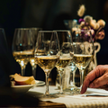Wine glasses on a table at a formal dinner, with a hand writing on a notepad and flowers in the background