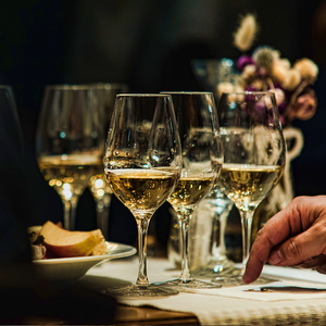 Wine glasses on a table at a formal dinner, with a hand writing on a notepad and flowers in the background