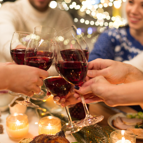 People toasting with red wine glasses at a candlelit dinner table with string lights