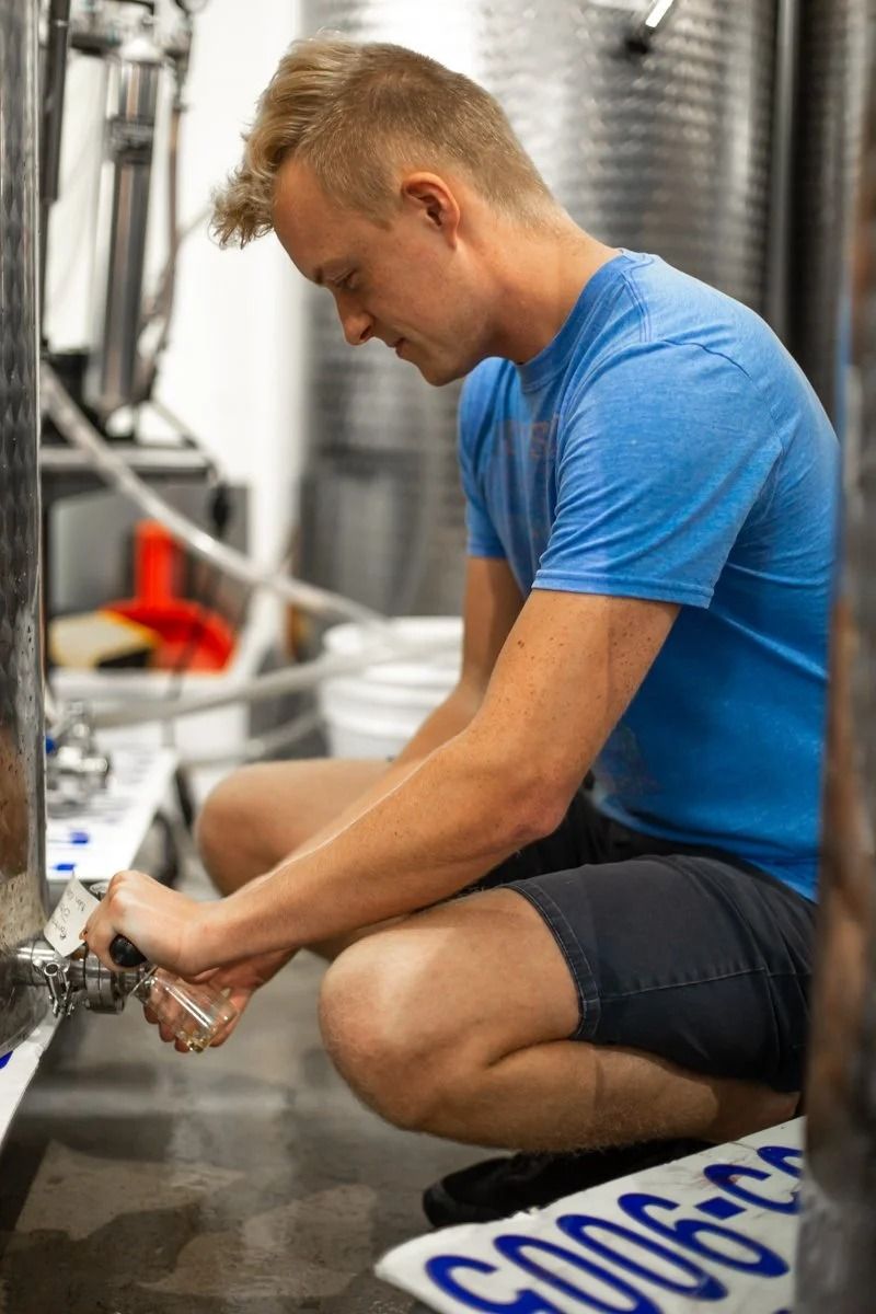 Man in blue shirt crouches to open a valve in a stainless-steel industrial facility