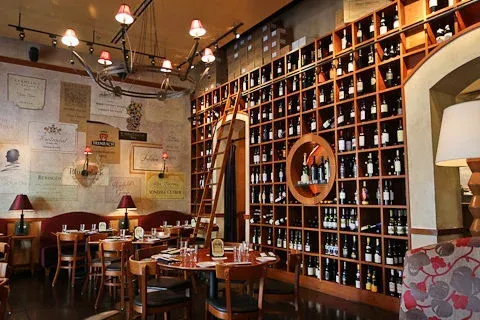 Cozy café interior with wooden tables, red lamps, and a wall of wine bottles.