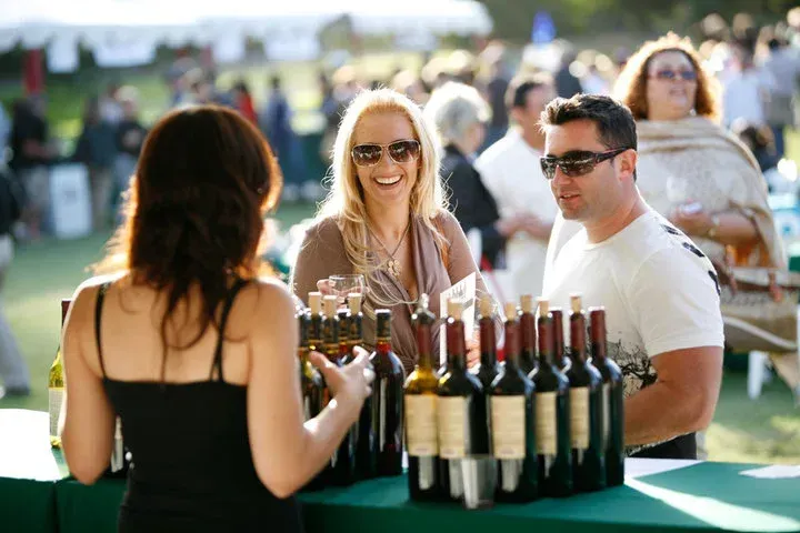 People tasting wine at an outdoor table with several bottles on display