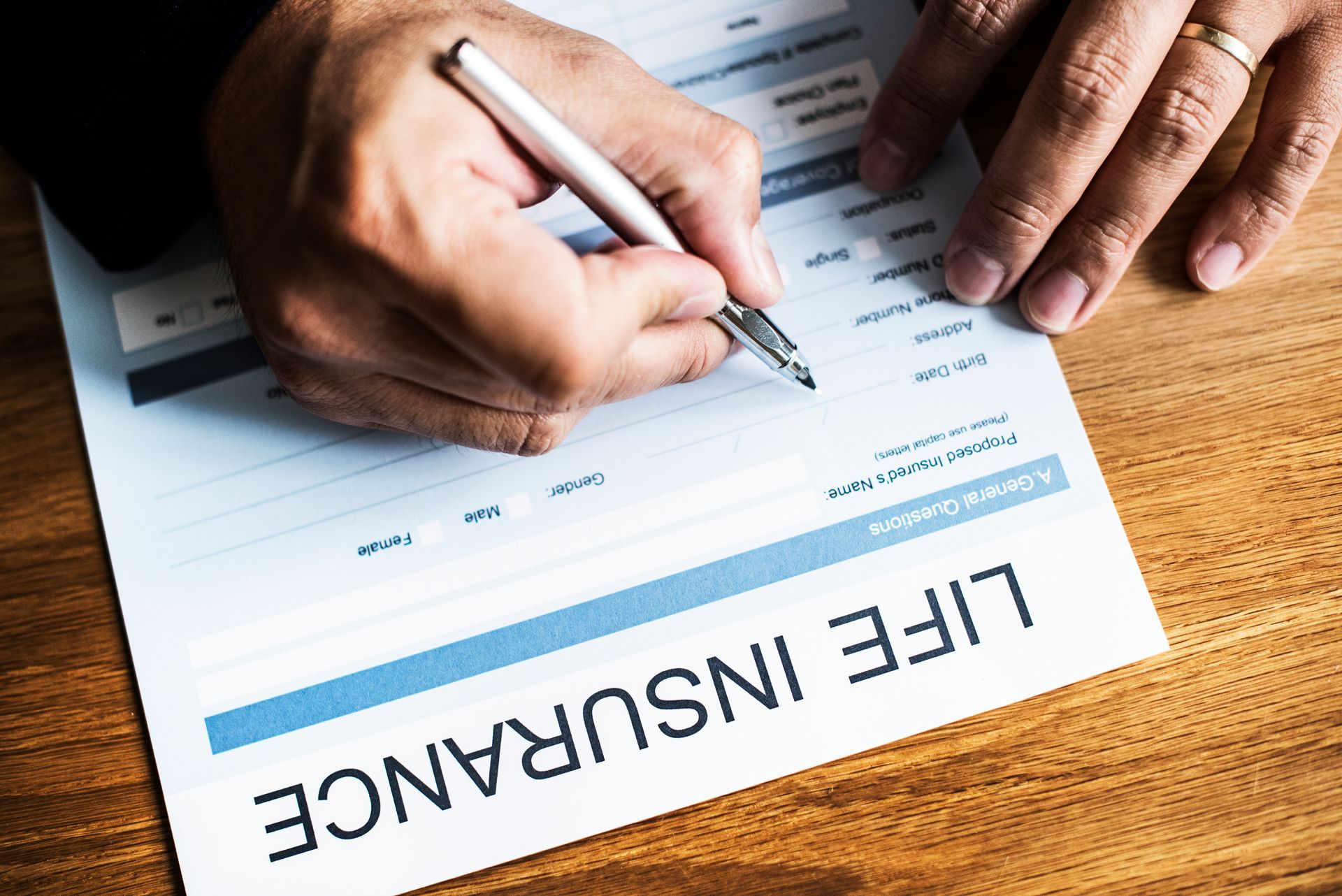 Close-up of a man's hands signing life insurance coverage documents on a wooden desk.
