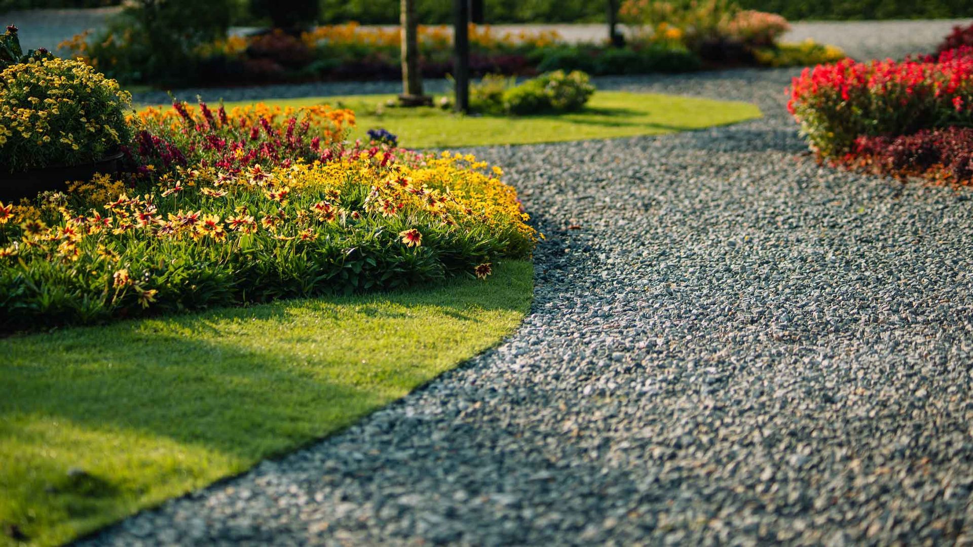 Curved gravel garden path bordered by green lawn and colorful flower beds