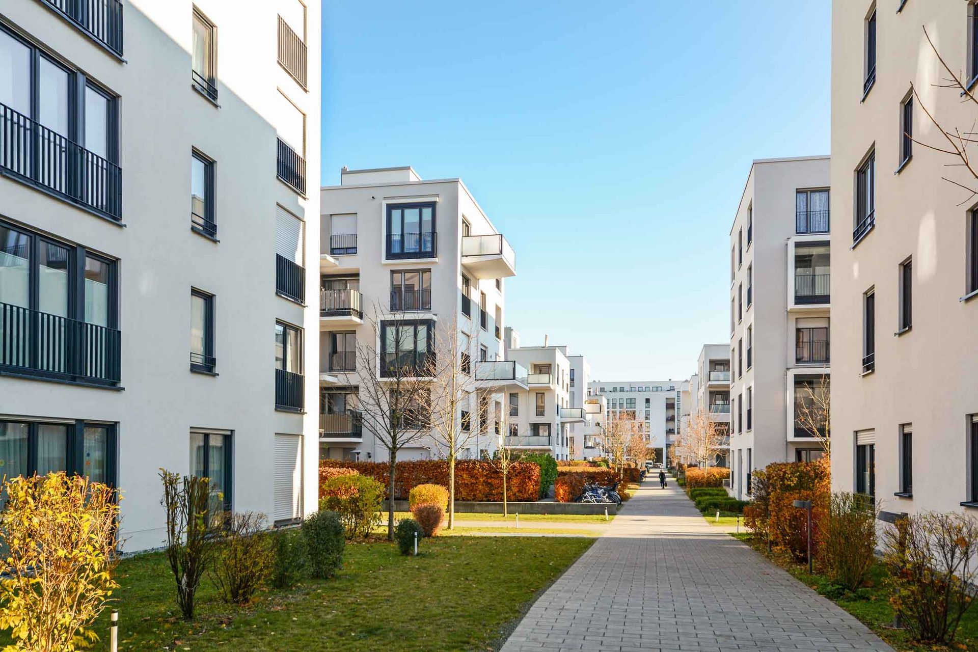 Modern apartment buildings lining a landscaped courtyard with a central path and autumn-colored trees