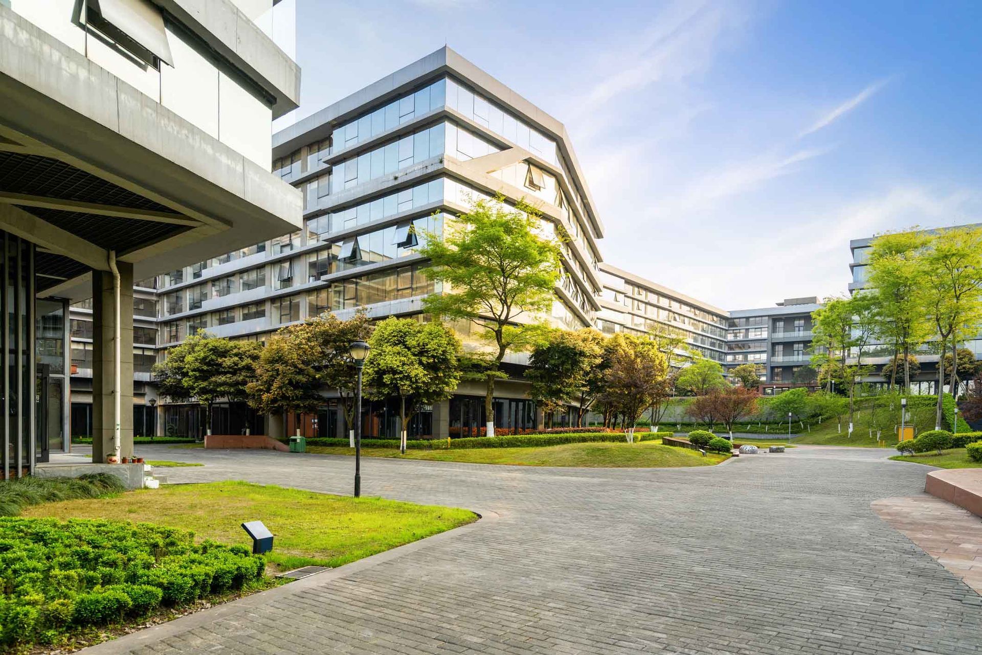 Modern office campus courtyard with glass buildings, trees, and a curved paved walkway