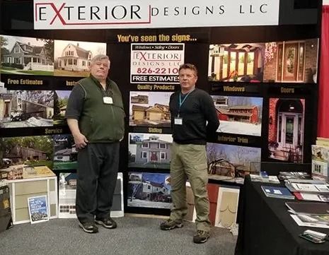 Two people standing at an Exterior Designs LLC trade show booth with brochures and product displays