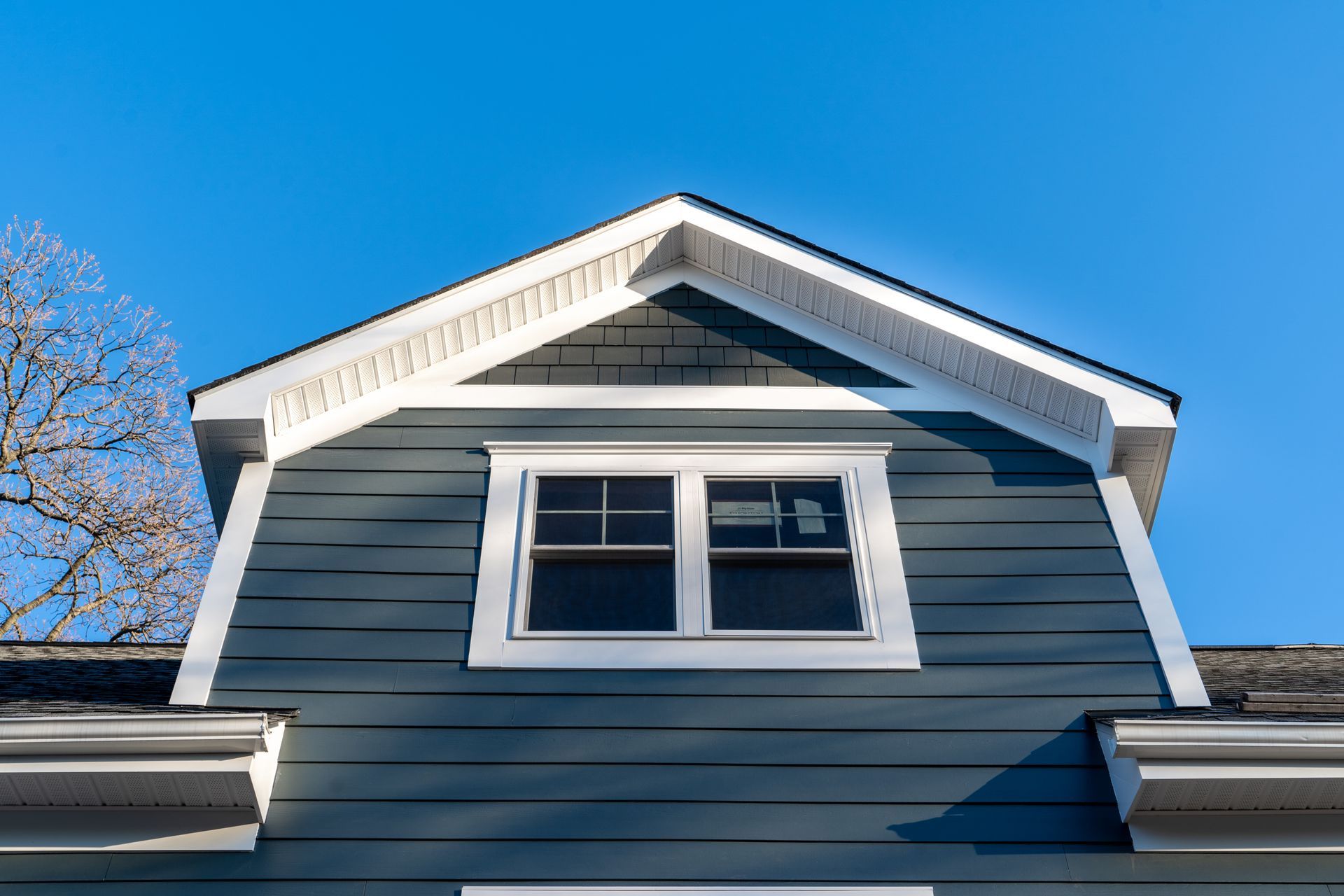White-trimmed dormer window on blue house siding against a clear blue sky