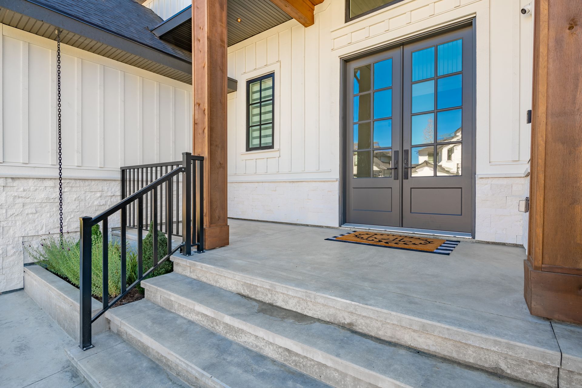Front porch with concrete steps, black railing, and gray double doors on a white house