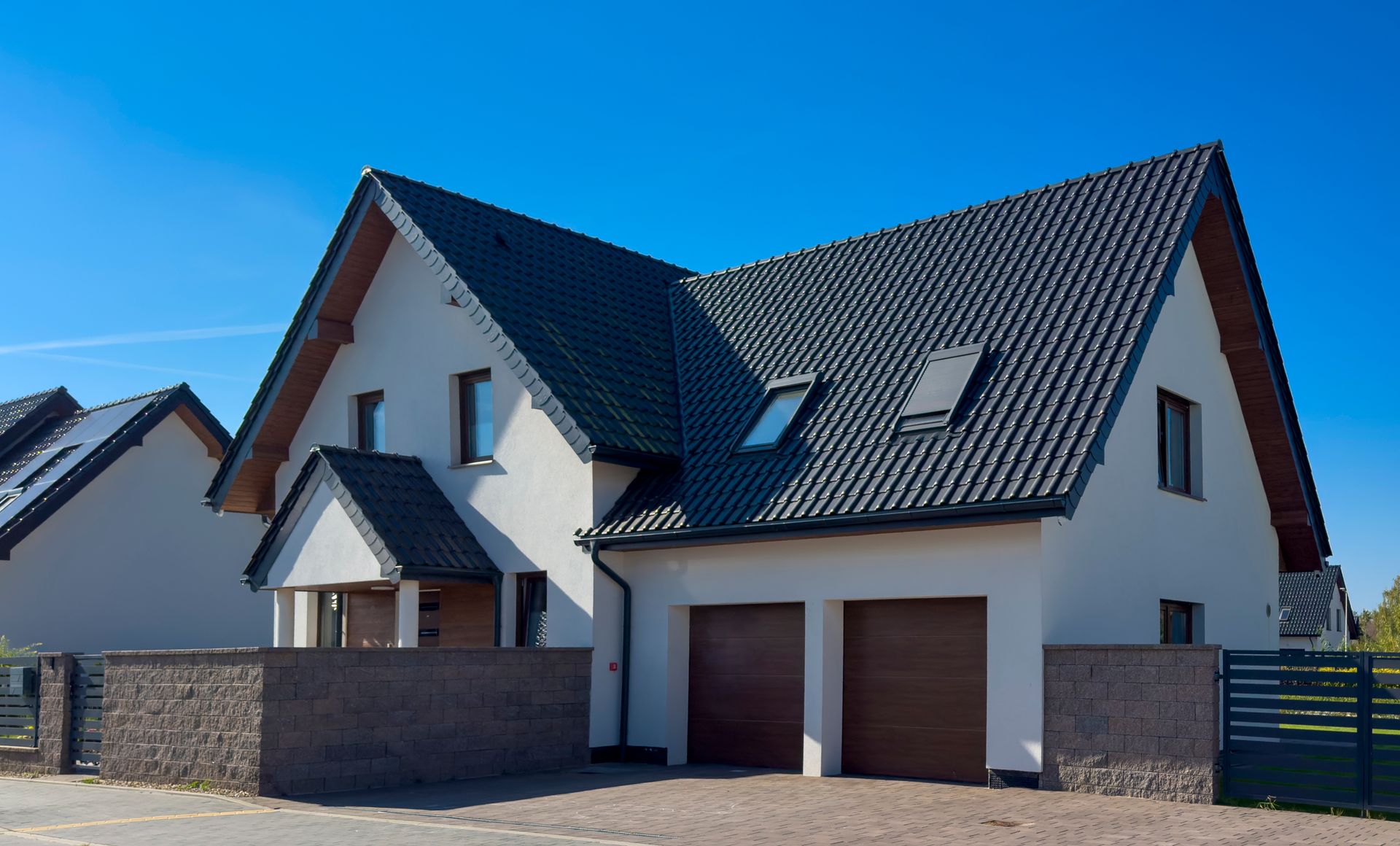 Modern two-story house with dark roof, white walls, and a double garage under a blue sky