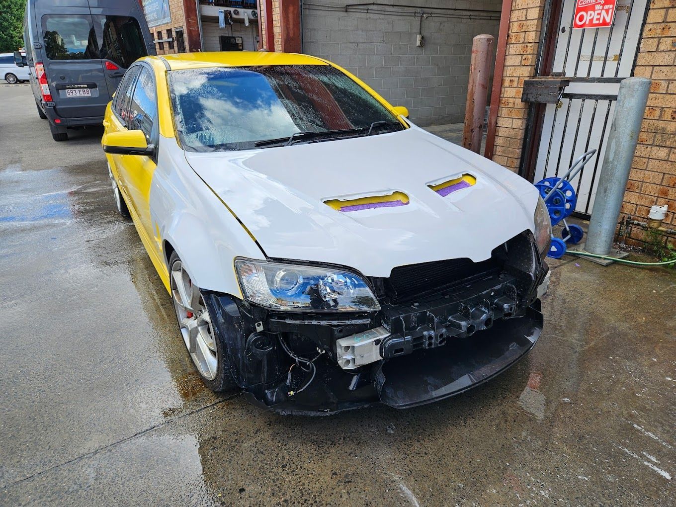 Damaged white-and-yellow sports car with a crushed front bumper parked in a wet alley