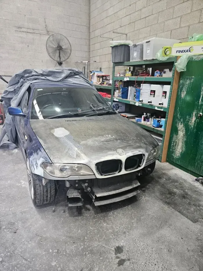 Dust-covered car in a workshop garage beside shelves and a wall fan