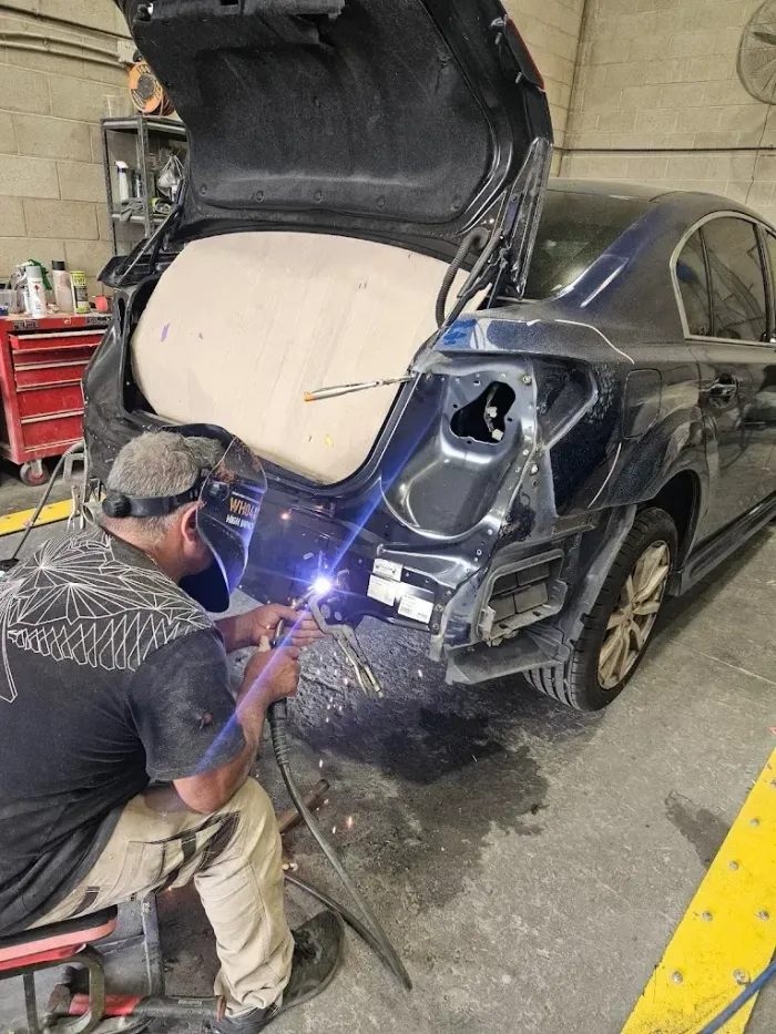 Mechanic welding a blue car in a garage, rear panel removed and trunk open