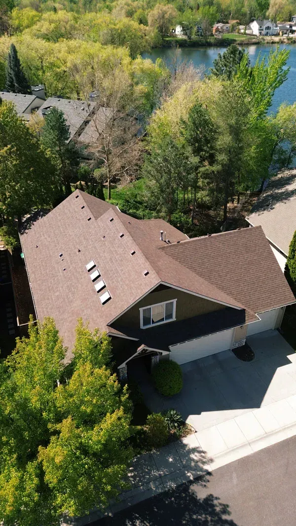 Aerial view of a brown-roofed house surrounded by green trees near a lake.