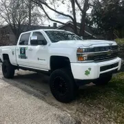 White lifted pickup truck with black wheels parked on a roadside, with green shamrock decals on the door.