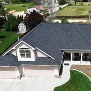 Aerial view of a suburban house with dark roof, light siding, driveway, and front lawn.