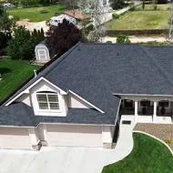 Aerial view of a suburban house with dark roof, light siding, driveway, and front lawn.