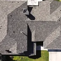 Aerial view of a house roof with gray shingles and a small green lawn below.
