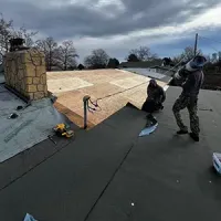Workers roofing a house, installing plywood under overcast skies.