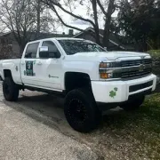 White lifted pickup truck with black wheels parked on a roadside, with green shamrock decals on the door.