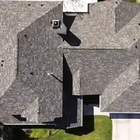 Aerial view of a house roof with gray shingles and a small green lawn below.