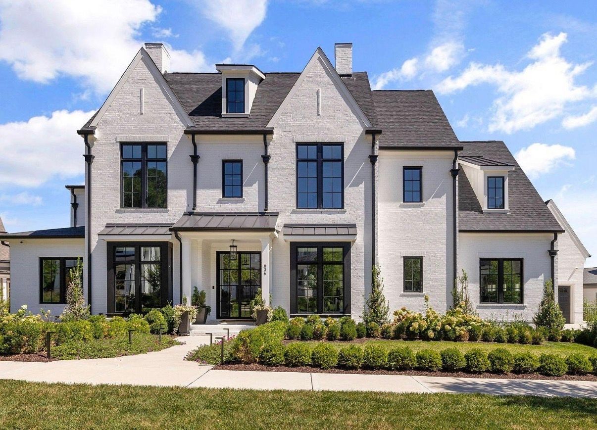 Large modern white stone house with gabled roof, black-framed windows, and landscaped front yard