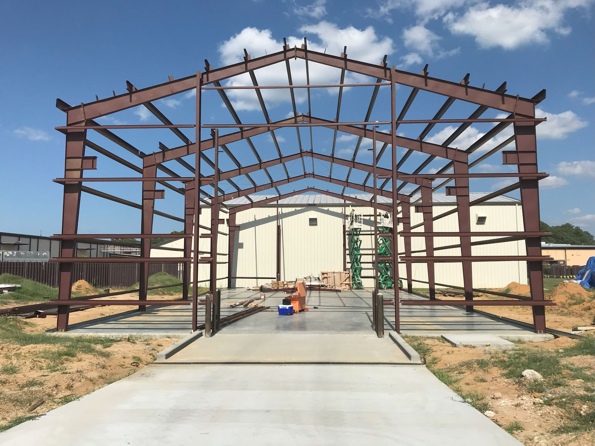Steel frame of a building under construction, brown against a light blue sky.
