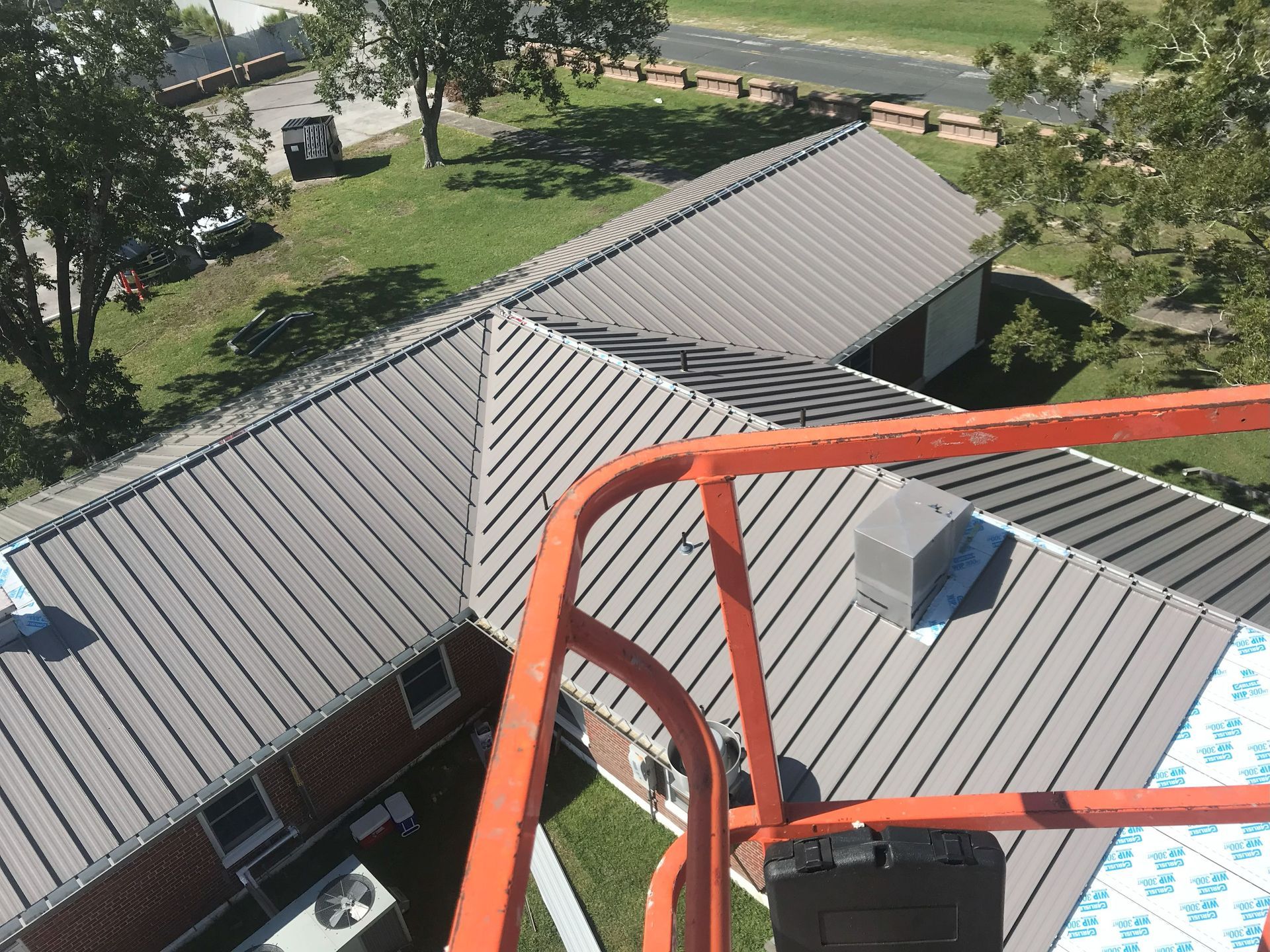 Aerial view of a gray metal roof with ridgelines; an orange lift frame is in the foreground.
