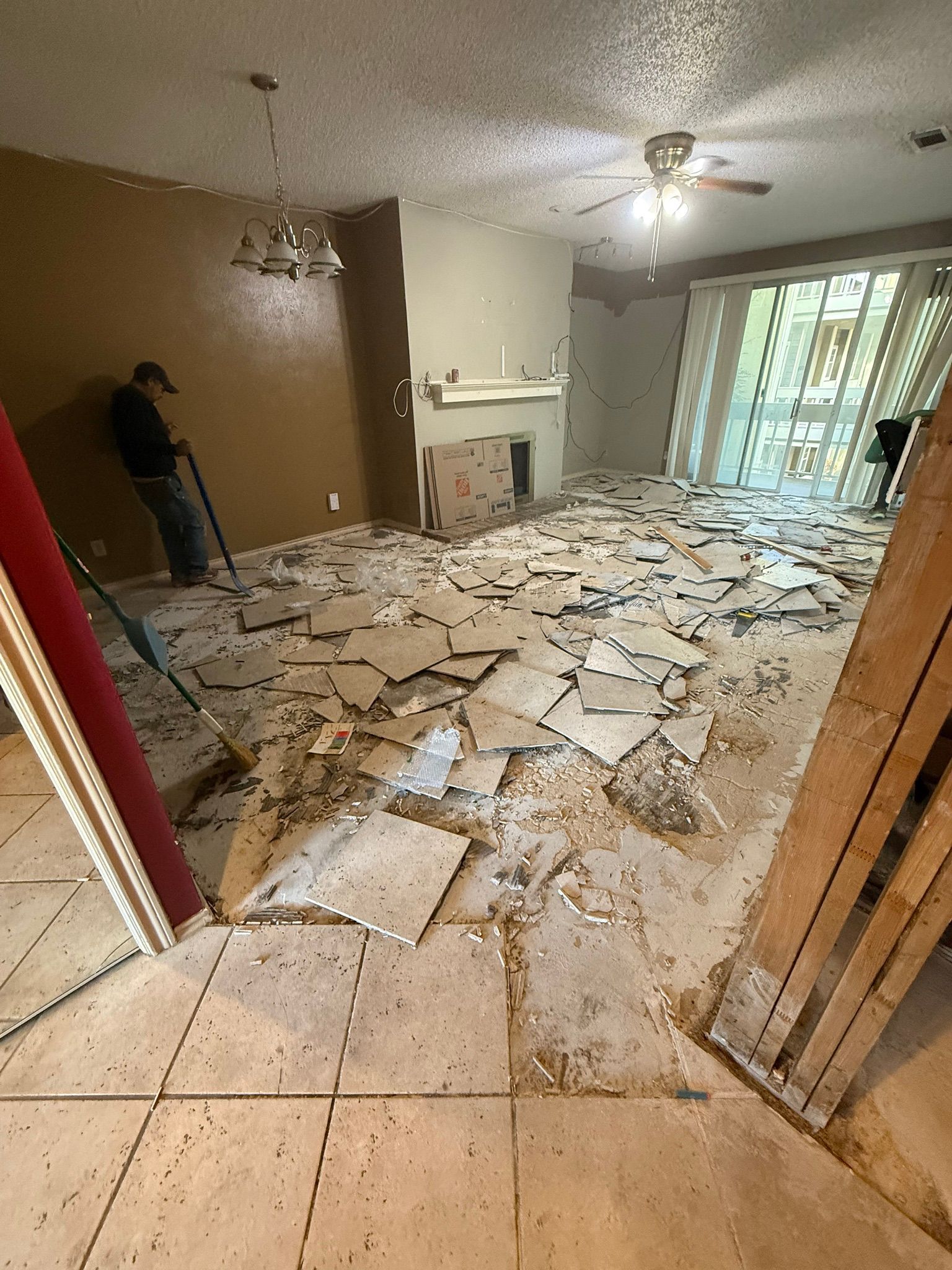 Room under renovation with torn-up tile flooring. A person leans against a wall.