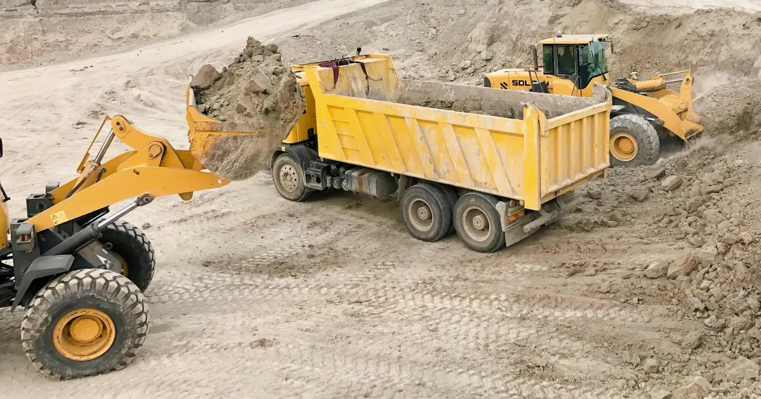 Yellow dump truck and loader working in a sandy construction site Yellow dump truck and loader working in a sandy construction site