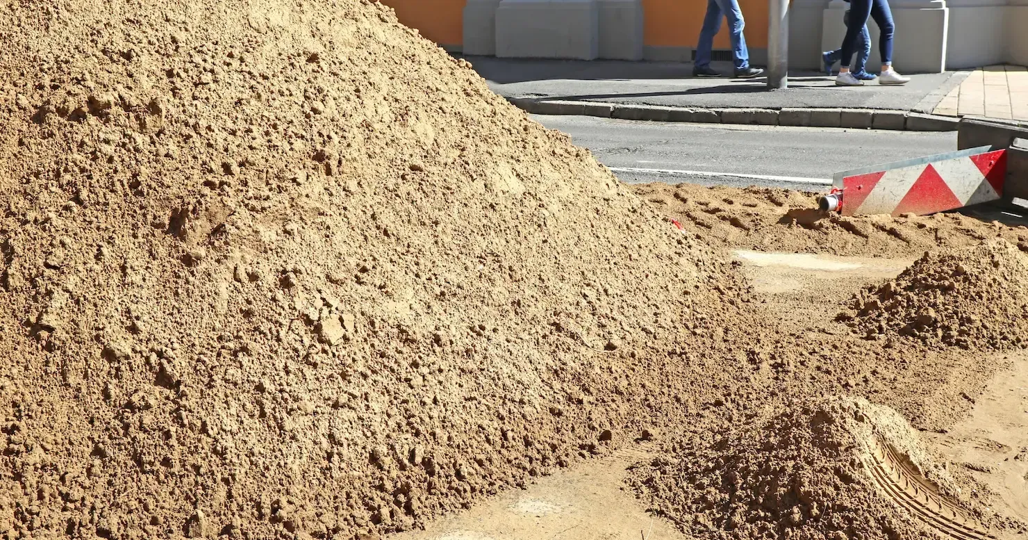 Large pile of sand at a construction site with a road barrier and a few people in the background Large pile of sand at a construction site with a road barrier and a few people in the background