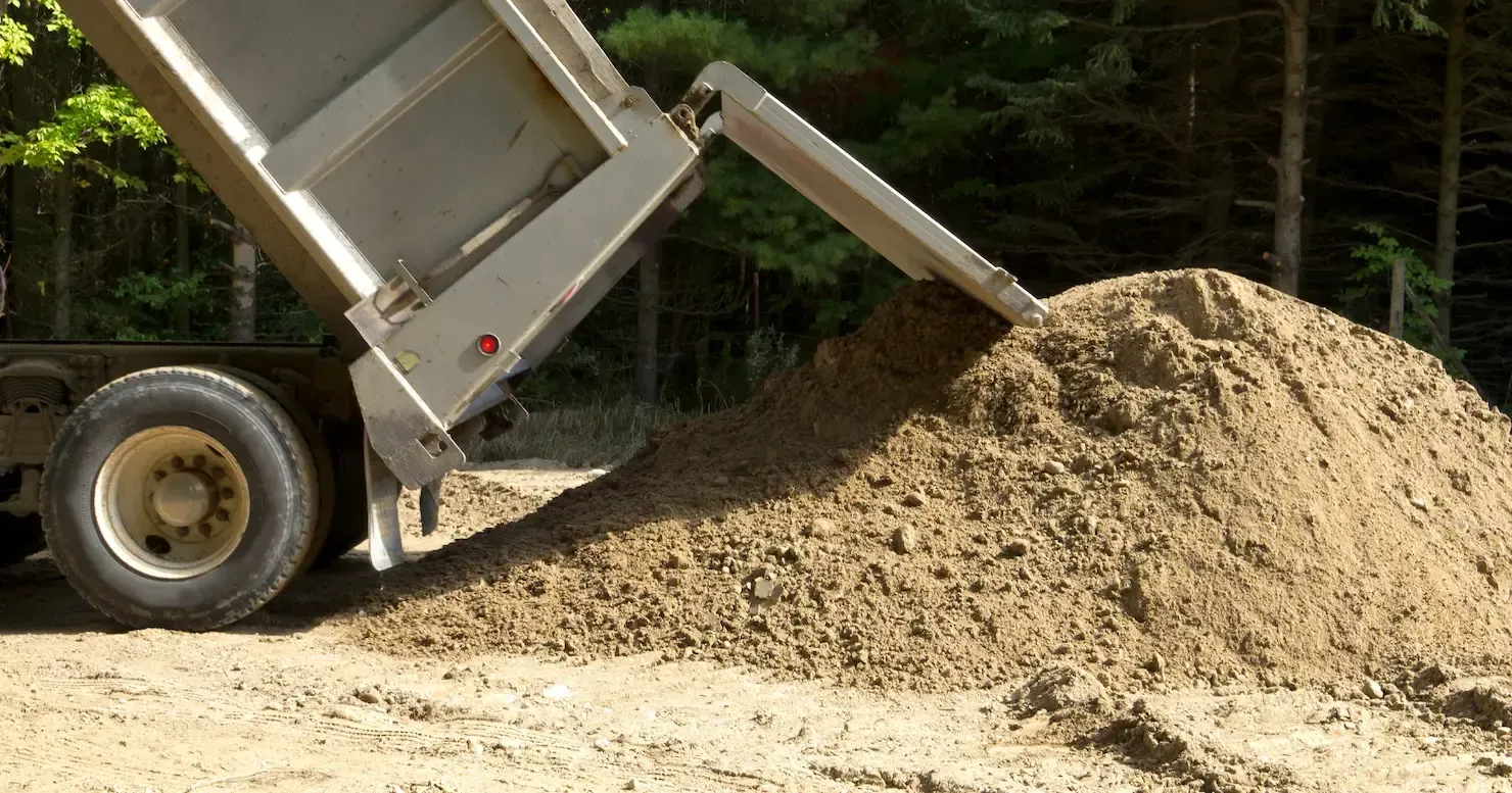 Dump truck unloading a large pile of sand or gravel in a wooded area Dump truck unloading a large pile of sand or gravel in a wooded area