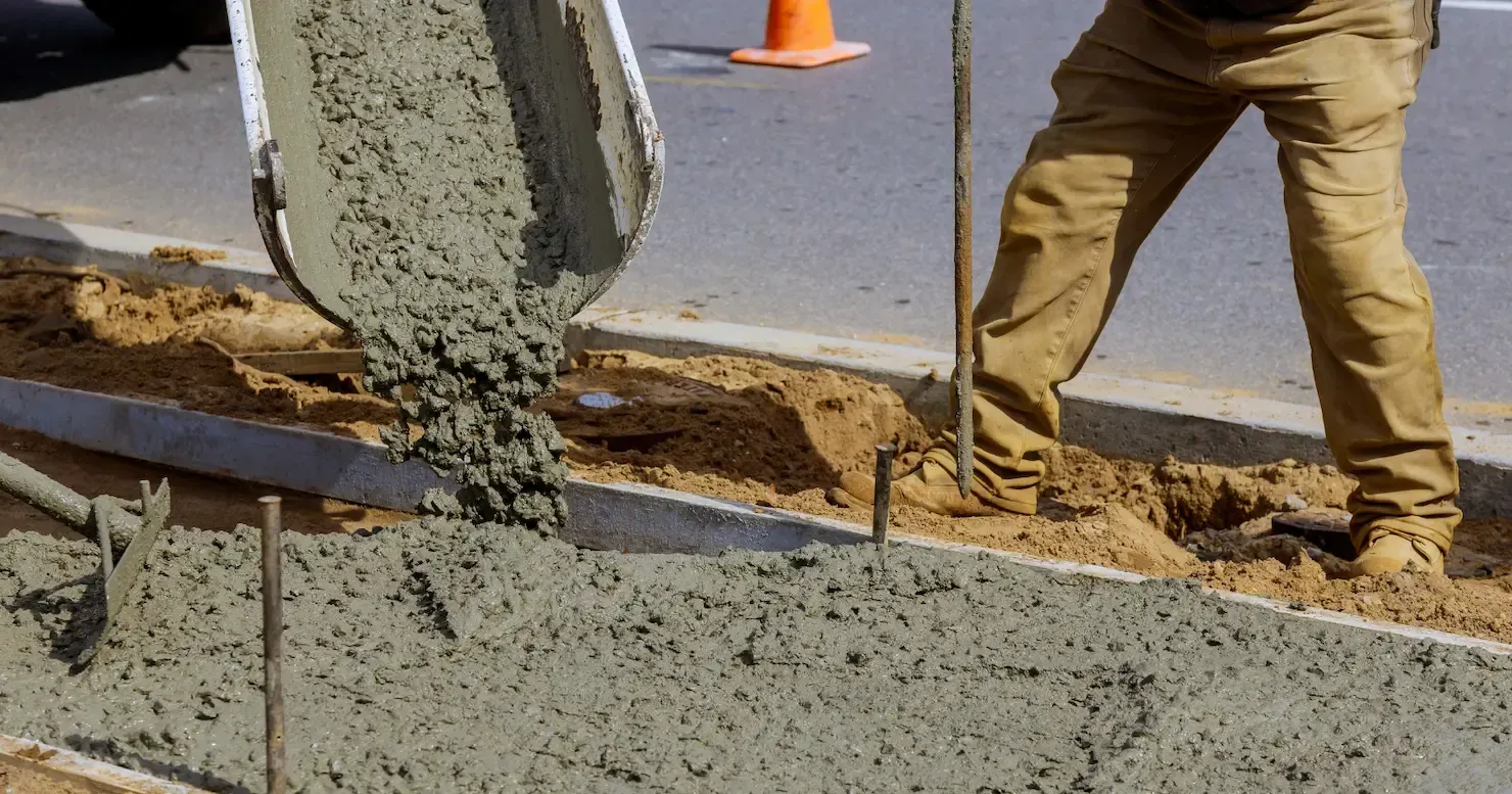 Worker smoothing fresh concrete slab at a construction site with mountains in the background