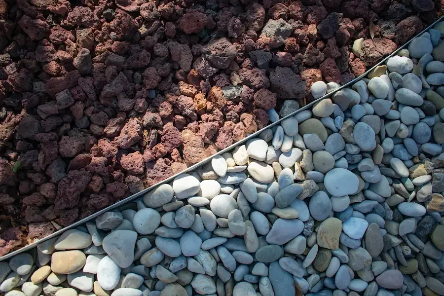 Diagonal border between dark red rocks and smooth gray pebbles in sunlight