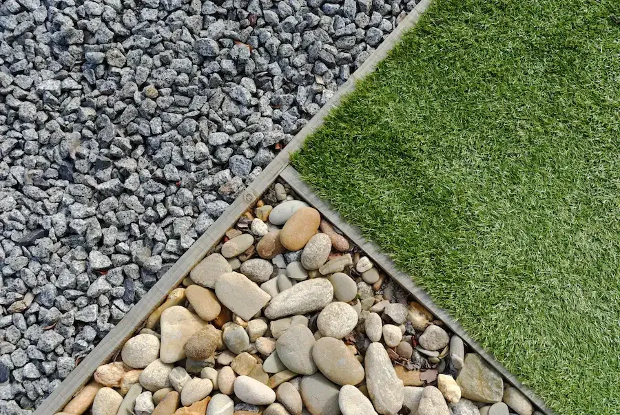 Three-way border between gray gravel, tan river stones, and green grass panels