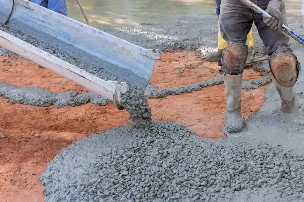Construction workers pouring wet concrete beside a curb on a road site