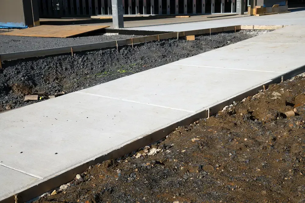 New concrete sidewalk beside a raised wooden deck and gravel path under construction
