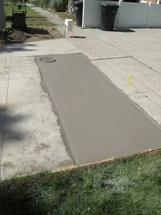 Freshly poured concrete sidewalk ramp beside a driveway with survey markers and grassy edges