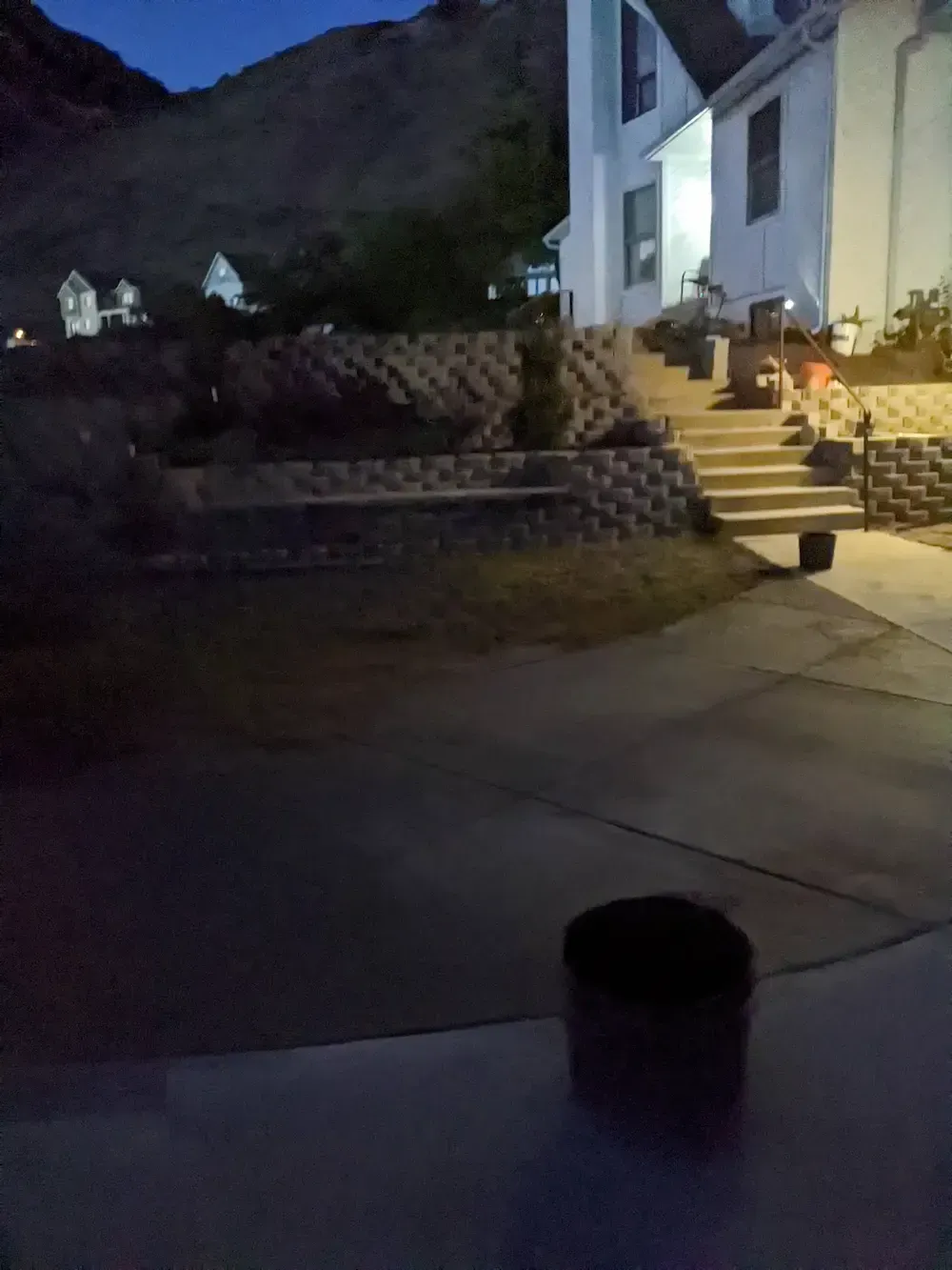 Nighttime view of a house entryway with lit stairs, a driveway, and mountains in the background