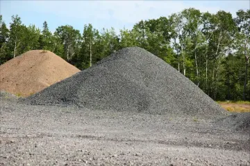 Piles of gravel and sand in a construction yard with trees in the background