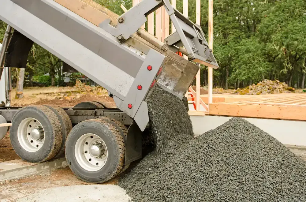 Dump truck unloading gray gravel at a construction site
