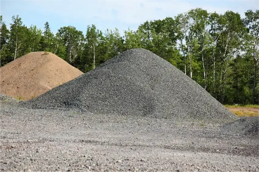 Dump truck unloading gravel at a road construction site, with workers and heavy equipment nearby