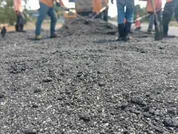 Workers paving a road with fresh asphalt, shovels visible in the background