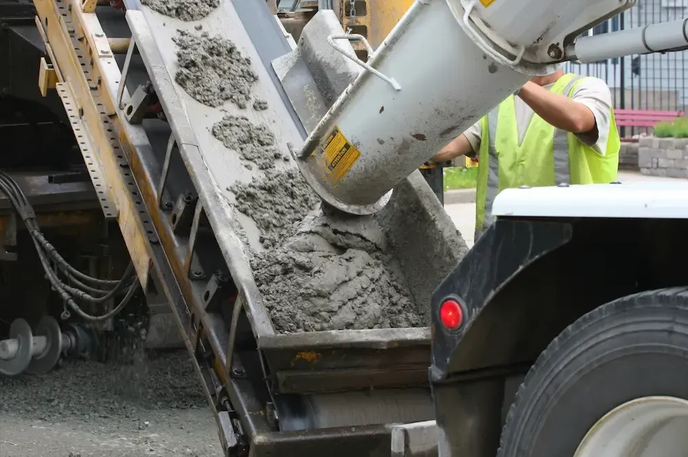 Concrete being poured from a truck chute onto a construction site, with a worker nearby